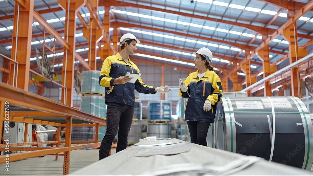 Male and female industrial engineers in hard hats discuss new project standing and talking at industry manufacturing factory