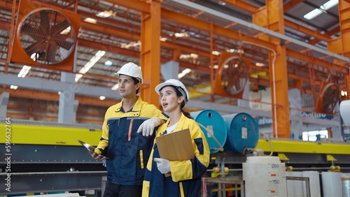 Two manufacturing employees in hard hats walk in steel metal manufacturing factory plant industry