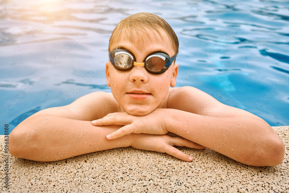 Naklejka premium Smiling boy portrait in swimming goggles, Child swim in the pool, sunbathes, swimming in hot summer day. Sport, Travel, Holidays 
