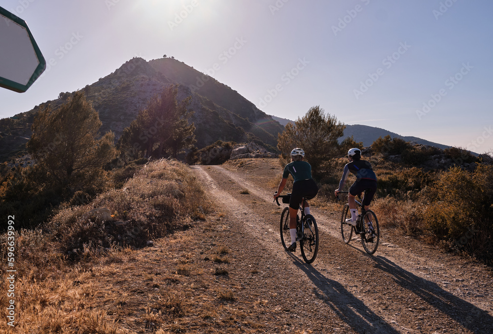 Back view of professional gravel cyclists riding uphill with mountain view at sunset. Alicante region in Spain Back view of professional gravel cyclists riding uphill with mountain view at sunset. Alicante region in Spain