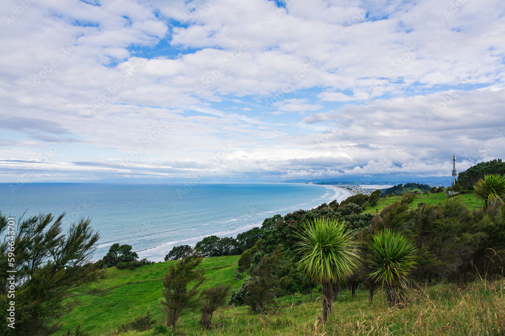 Breathtaking aerial view over vast ocean beach surrounded by distant mountains. Mist rising over water. Patches of blue sky seen through the clouds. Whakatane, North Island, New Zealand