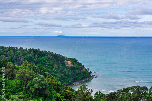 Beautiful sea landscape. Looking down a green cove with azure waves rolling over coastal rocks Active volcano White Island can be seen steaming at the horizon. Whakatane, North Island, New Zealand