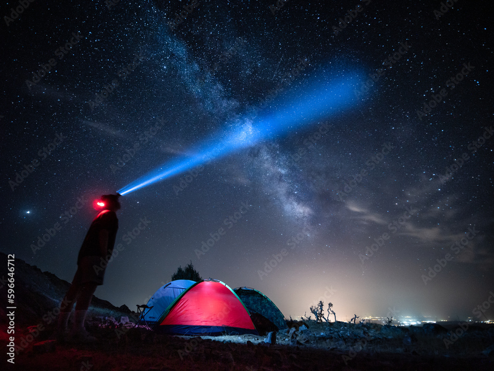 Persona con una linterna bajo las estrellas acampa en la montaña con tienda de campaña. - obrazy, fototapety, plakaty 