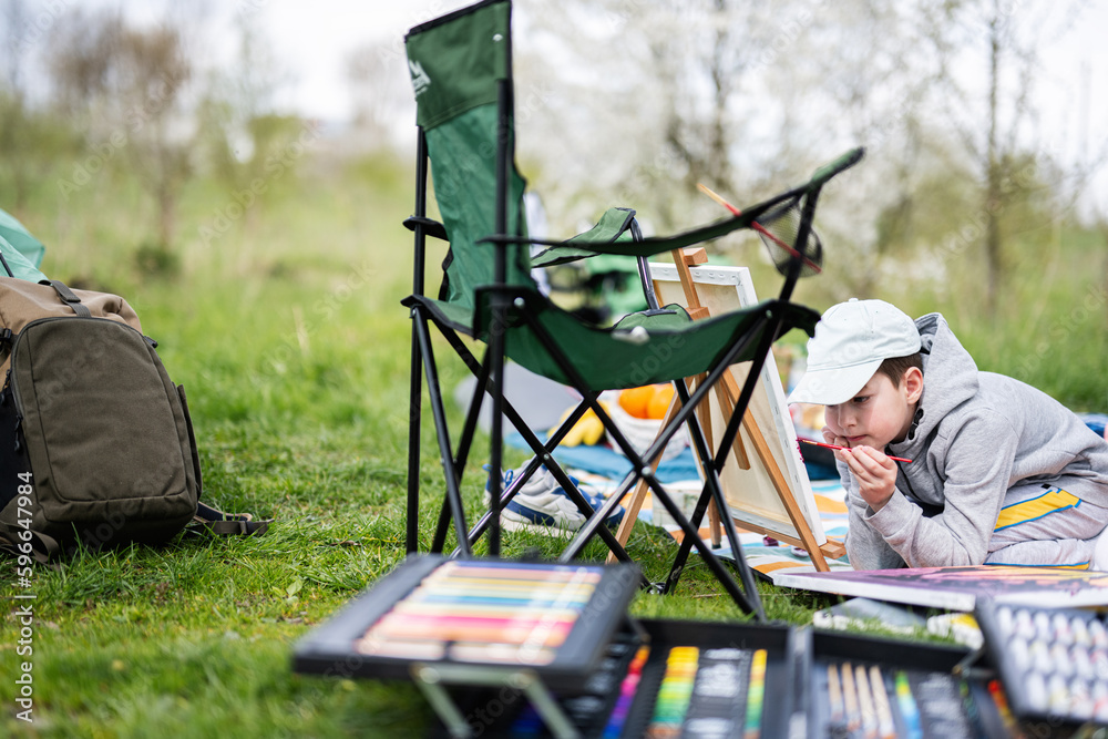 Boy enjoying outdoor on picnic blanket and painting on canvas at garden spring park, relaxation. Boy enjoying outdoor on picnic blanket and painting on canvas at garden spring park, relaxation.