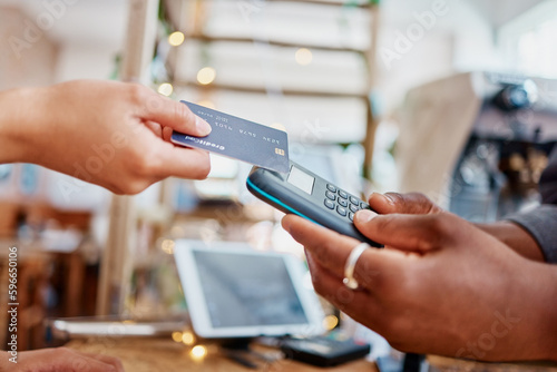 Closeup of unknown mixed race customer using a wireless credit card machine to pay for her coffee. African american barista assisting a woman in a cafe. Contactless paying system during covid pandemic