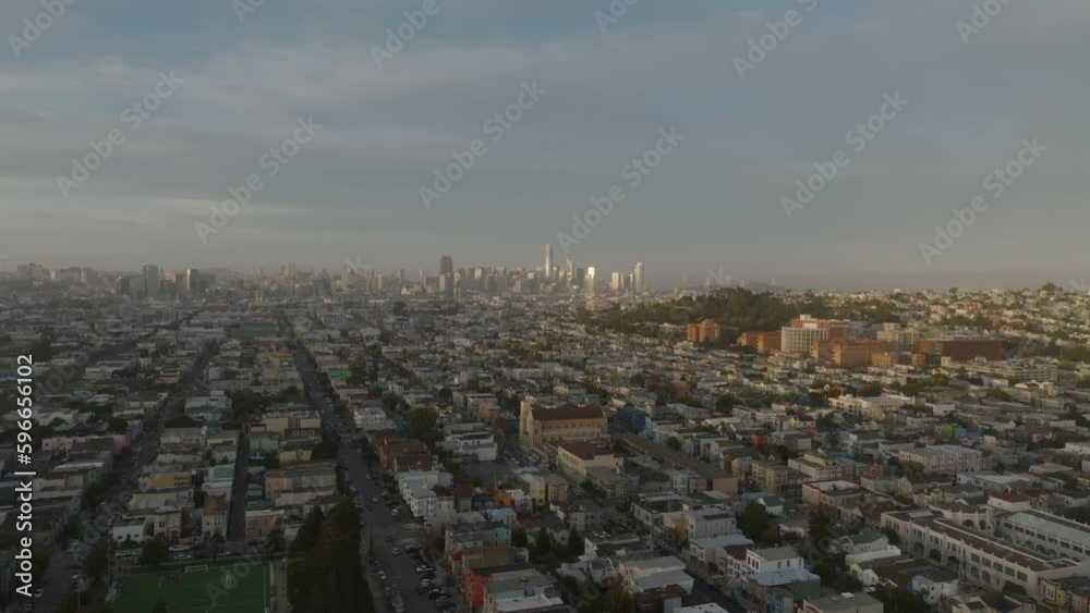 Fly above residential houses along long straight streets in urban borough. Modern high rise office buildings in distance.