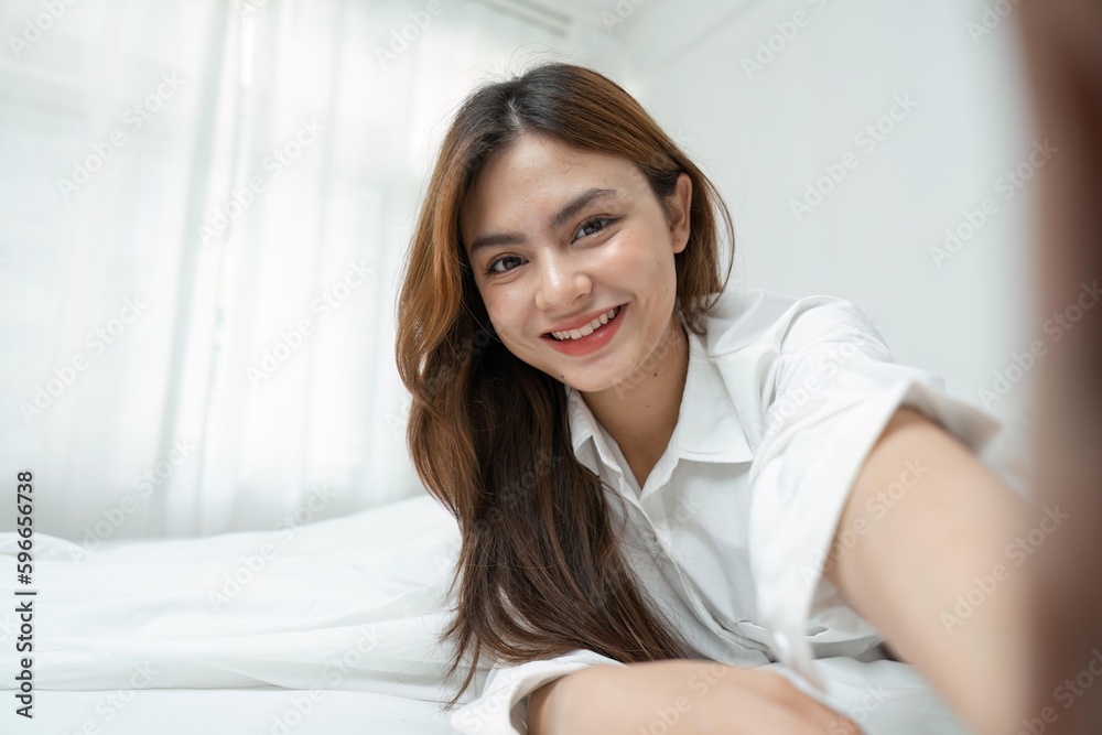 Young woman using camera of smartphone taking sunny selfie at home Young woman using camera of smartphone taking sunny selfie at home