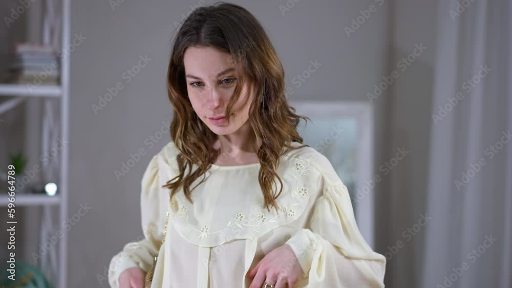 Live camera moves down along slim confident woman trying on outfit indoors. Happy satisfied Caucasian stylish lady in living room at home