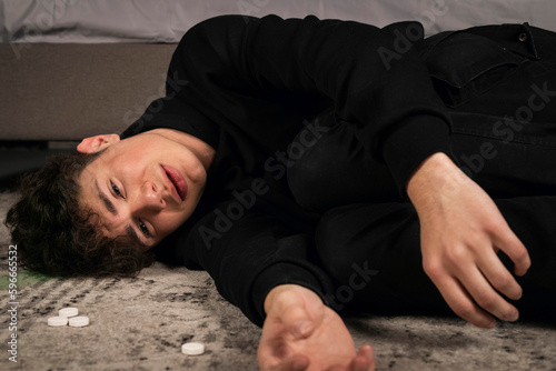 A severely depressed guy, lying on the floor among pills and a bottle of alcohol. A young man in a hard mental condition. alcohol and drugs addiction.