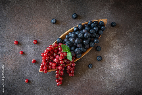 Mix of berries - blueberries and red current on wooden dish on dark brown background 