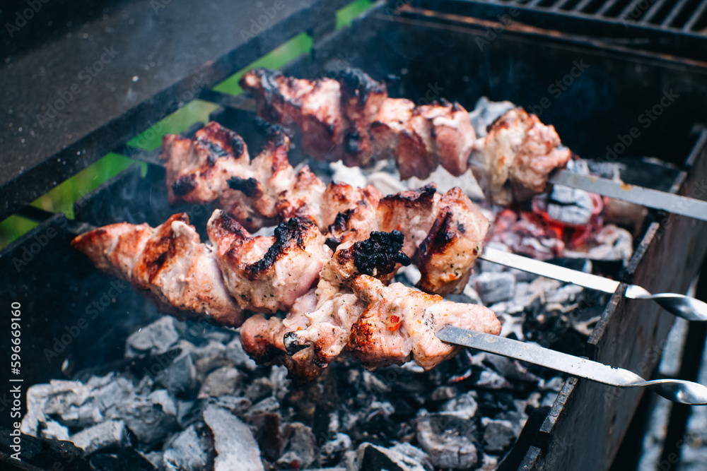 Frying meat pork on the grill. Shish kebab for summer party. Shashlik on wooden panels and open fire.