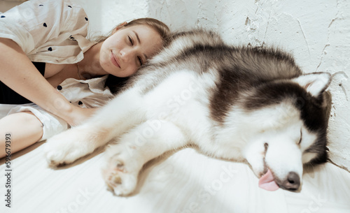 Young woman and her dog carefree at home background. Beautiful girl have fun playing with her adorable pet friend at leisure. Friendly malamute happy cuddle and sleep with owner who love and care.