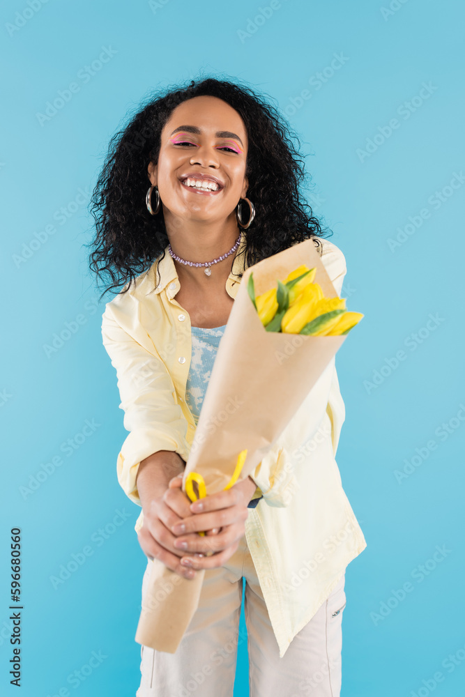 overjoyed african american woman holding bouquet of yellow tulips in outstretched hands isolated on blue. overjoyed african american woman holding bouquet of yellow tulips in outstretched hands isolated on blue.
