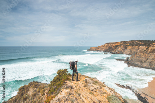 Hiker and adventurer stand on a rugged rock and cliff coastline and enjoy the view on the Atlantic Ocean in the west of Portugal in the famous tourist region of the Algarve