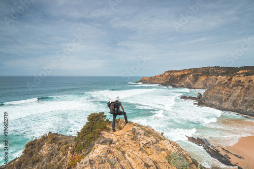 Hiker and adventurer stand on a rugged rock and cliff coastline and enjoy the view on the Atlantic Ocean in the west of Portugal in the famous tourist region of the Algarve
