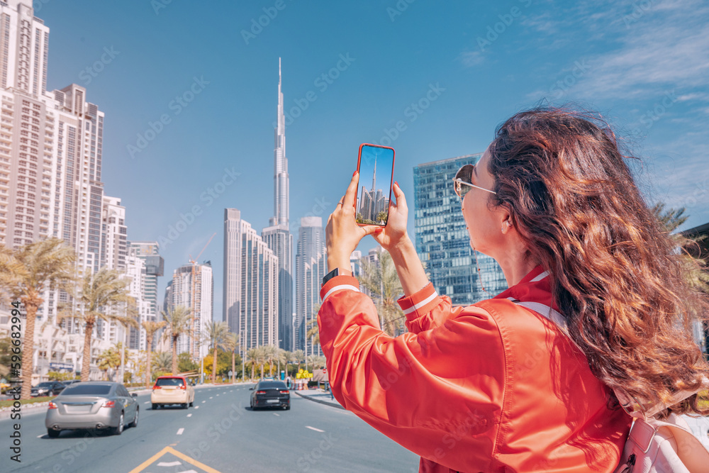 Tourist happy girl taking photos for her travel blog, in Dubai downtown district against background of the Burj Khalifa highest skyscraper