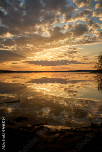 Bright orange fiery sunset with a reflection in the water on the shore of the bay
