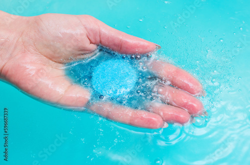 Fototapeta Naklejka Na Ścianę i Meble -  Hand of woman, having pampering bath, holding blue fizzing bath bomb.