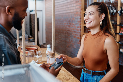 Happy hispanic customer paying for a meal in a restaurant using a nfc machine and credit card. Smiling young woman making a purchase in a store with her debit card and a pos machine. Woman paying bill photo