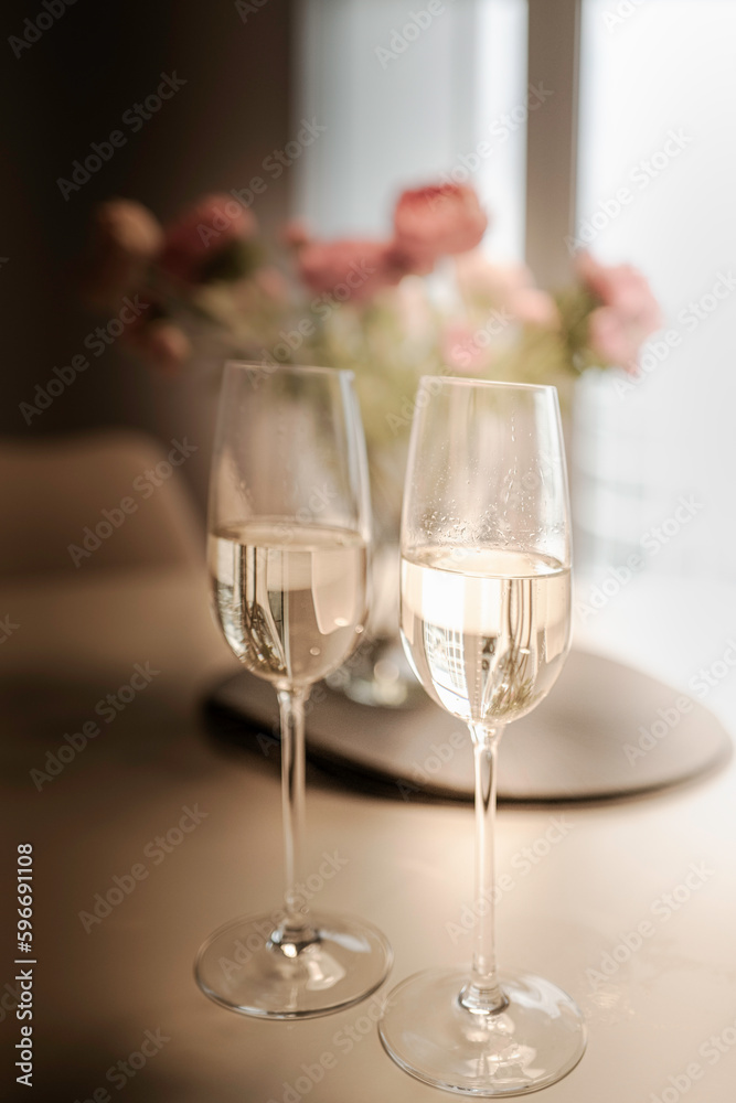 Two glasses of champagne with defocused flowers in the background and softly illuminated windows Two glasses of champagne with defocused flowers in the background and softly illuminated windows
