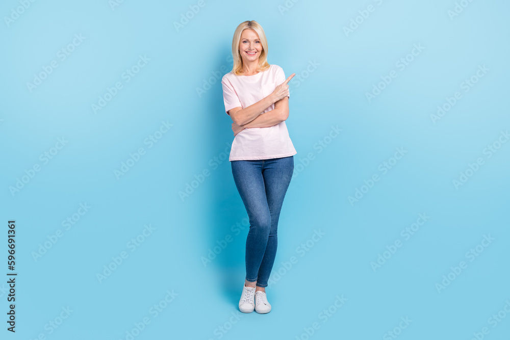Full length photo of satisfied person dressed white t-shirt pants indicating at discount empty space isolated on blue color background Full length photo of satisfied person dressed white t-shirt pants indicating at discount empty space isolated on blue color background