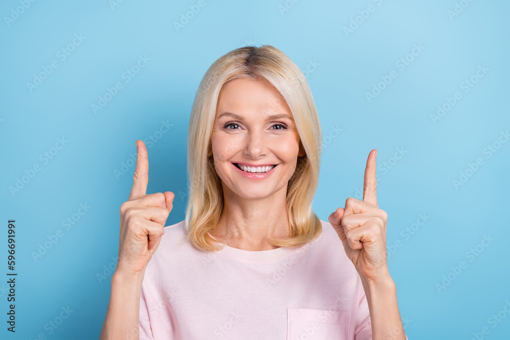 Photo of cheerful friendly lady beaming smile direct fingers up empty space isolated on blue color background Photo of cheerful friendly lady beaming smile direct fingers up empty space isolated on blue color background