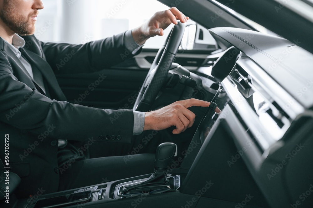 Turning the knobs. Man in formal business clothes is sitting in the modern automobile Turning the knobs. Man in formal business clothes is sitting in the modern automobile