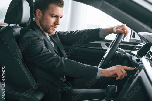 Turning the knobs. Man in formal business clothes is sitting in the modern automobile