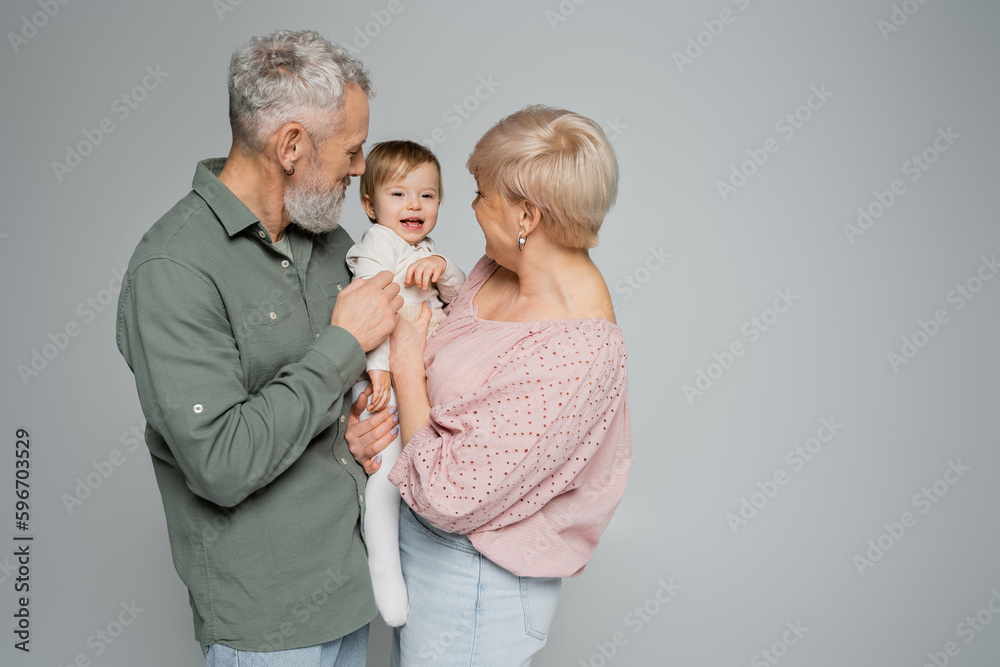 middle aged couple holding and hugging cheerful granddaughter isolated on grey. middle aged couple holding and hugging cheerful granddaughter isolated on grey.