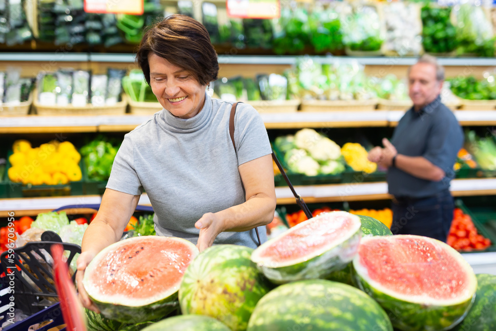 elderly woman chooses watermelon in fruit and vegetable section