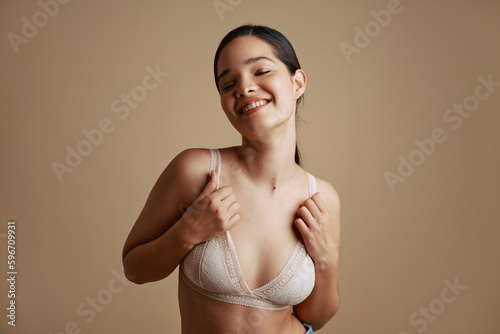 Smiling woman touching bra with closed eyes in studio photo