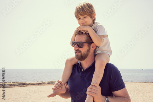 Obraz na plátně Son on fathers shoulders at the beach having fun at sunset together