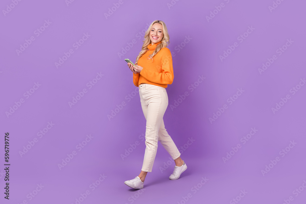 Full length profile photo of lovely positive person hold smart phone walking isolated on violet color background