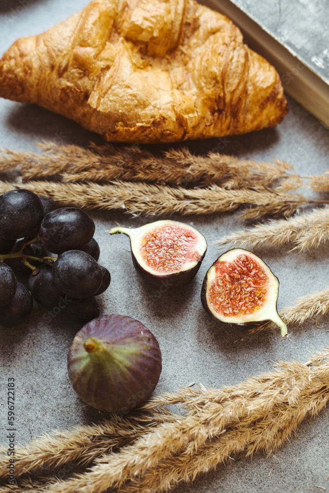 Autumn attributes. Croissant, dark grapes, book and figs on the grey table. Gold October Autumn attributes. Croissant, dark grapes, book and figs on the grey table. Gold October