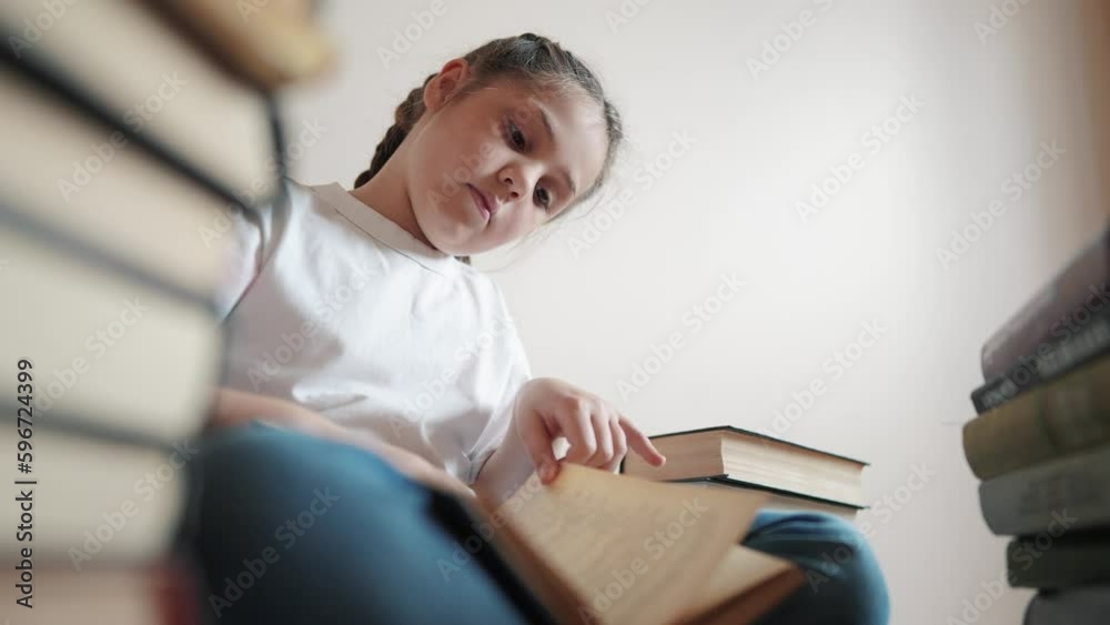 little girl in the library lifestyle reading a book. education school kid science concept. a child sits on the floor stacks of books flips through the pages reads studies. daughter reading a book little girl in the library lifestyle reading a book. education school kid science concept. a child sits on the floor stacks of books flips through the pages reads studies. daughter reading a book