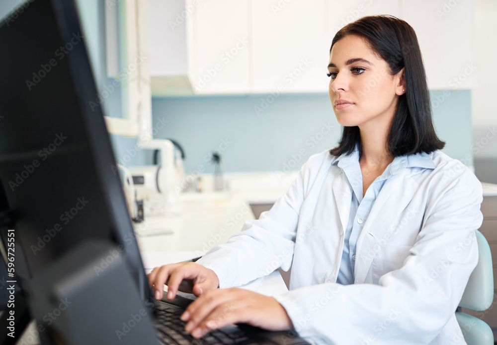 One confident and focused young caucasian doctor using a computer to browse the internet in a clinic. A medical professional wearing a labcoat and updating patient reports on a desktop in her hospital One confident and focused young caucasian doctor using a computer to browse the internet in a clinic. A medical professional wearing a labcoat and updating patient reports on a desktop in her hospital