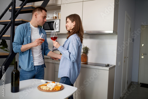 Happy celebration. Beautiful, loving couple standing in the kitchen, drinking red wine and talking. Morning eating. Concept of love, relationship, family, emotions, lifestyle, support and care