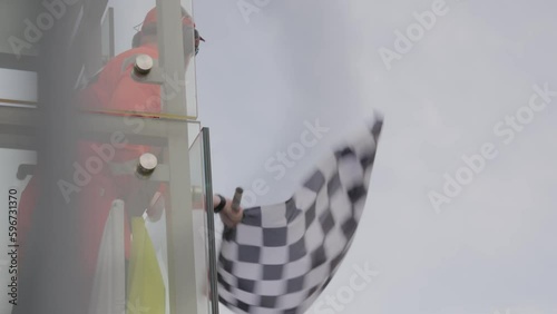 Man holding and waving Checkered race at finish line on a F1 raceway. Victory, achievement, success and sport concept. 