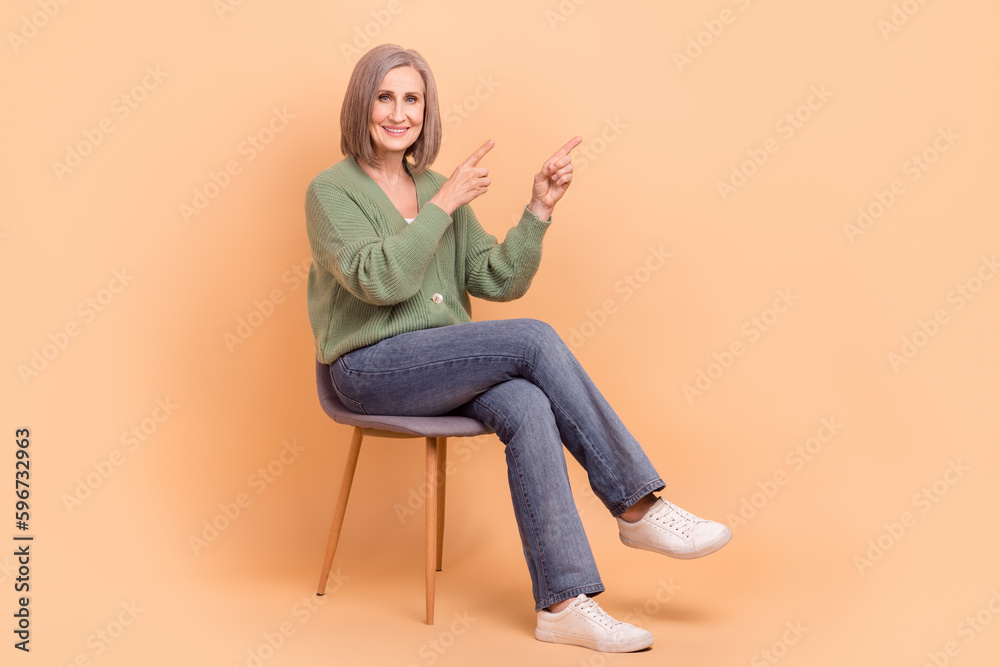 Full body cadre of comfortable armchair retired business lady trendy outfit point fingers mockup ikea isolated on beige color background Full body cadre of comfortable armchair retired business lady trendy outfit point fingers mockup ikea isolated on beige color background