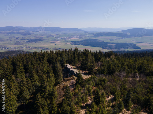 A beautiful drone view of forest with a rock and mountains in the background. Orlicke hory, Czechia.