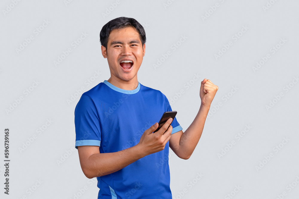 Happy man cheering excitedly in celebration after good news. Excited guy winner holding cellphone winning game online or investing trading, using mobile app celebrates victory success