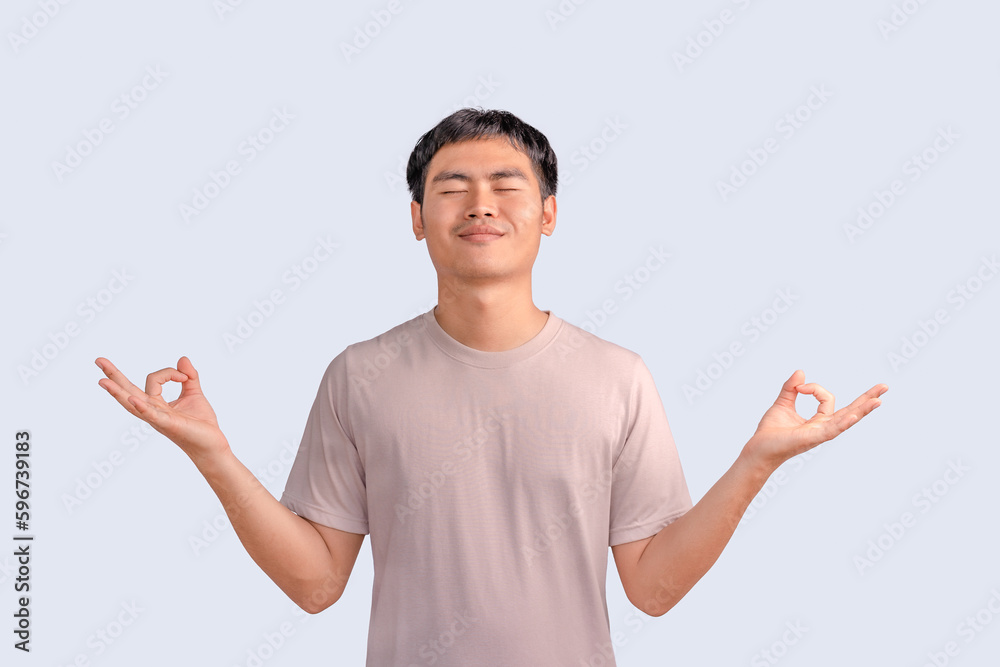 Happy smiling young man standing with closed eyes, having relaxation while meditating isolated on white background. Guy holds hands in yoga gesture, relaxing meditating, and trying to calm down.