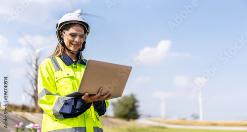 Caucasian woman engineer in uniform using laptop working stand near wind turbines farm, ecological energy industry, Environmental friendly for the future © TeTe Song