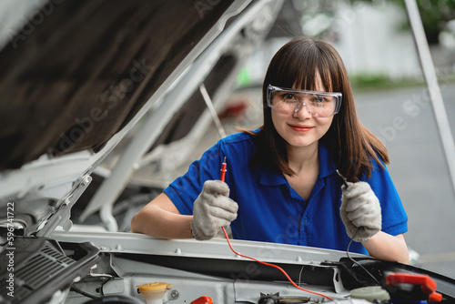Female auto mechanic opens car hood to inspect engine damage and perform professional maintenance He wore a blue uniform and inspected and repaired his car in the workshop.