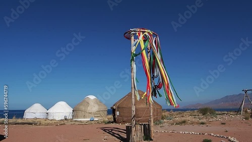 Traditional camp of nomads from yurts is set up on shore of lake Issyk-Kul. In center on platform there is pole with wheel and colored ribbons tied to it which developing in wind for Sabantuy holiday photo