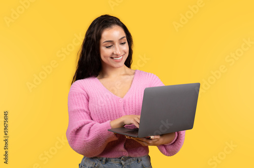 Cheerful millennial arab lady manager student in casual working on laptop isolated on yellow background