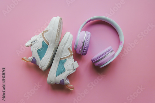 White children's sneakers and headphones on a pink background with copy space. Banner