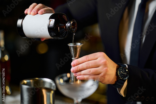 An unrecognisable bartender pours an ingredient from a bottle to make a cocktail . Creating delicious cocktails at the bar