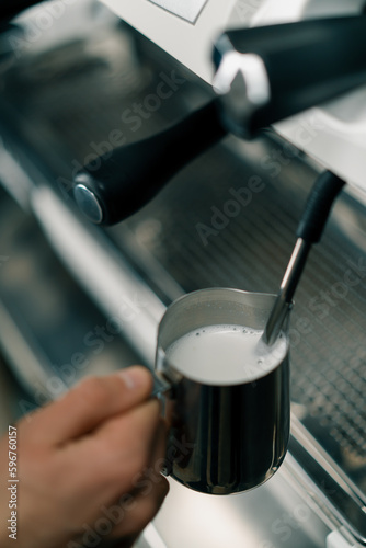 barista uses coffee machine and churns fresh milk to prepare latte or cappuccino in cafe for customer