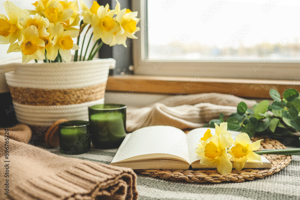 Open book, candle and basket with daffodils, spring cozy composition in home interior